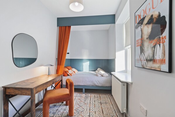 A bedroom with a bed, a desk, a chair, a mirror, and a poster on the wall.
