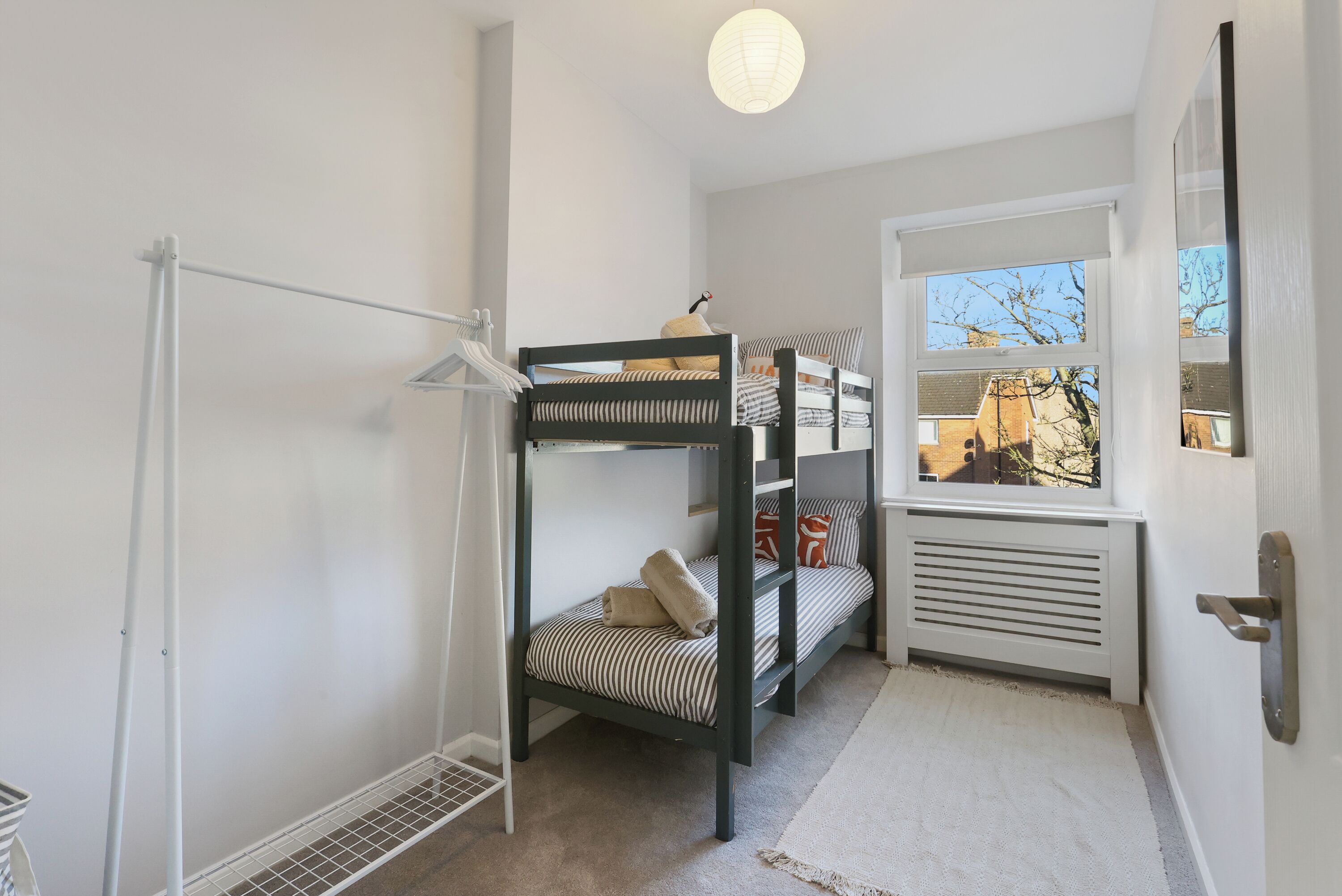 Habitación con literas, un radiador, una lámpara colgante y vistas al exterior por una ventana.