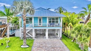 A two-story beachfront house with a blue roof, white exterior, and a balcony with white railings.