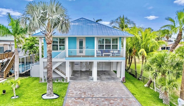 A two-story beachfront house with a blue roof, white exterior, and a balcony with white railings.