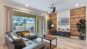 A modern living room with a leather sofa, a coffee table, and a TV. There is a sliding glass door leading to a balcony with outdoor furniture. - The Solterra Resort Retreat (Davenport)