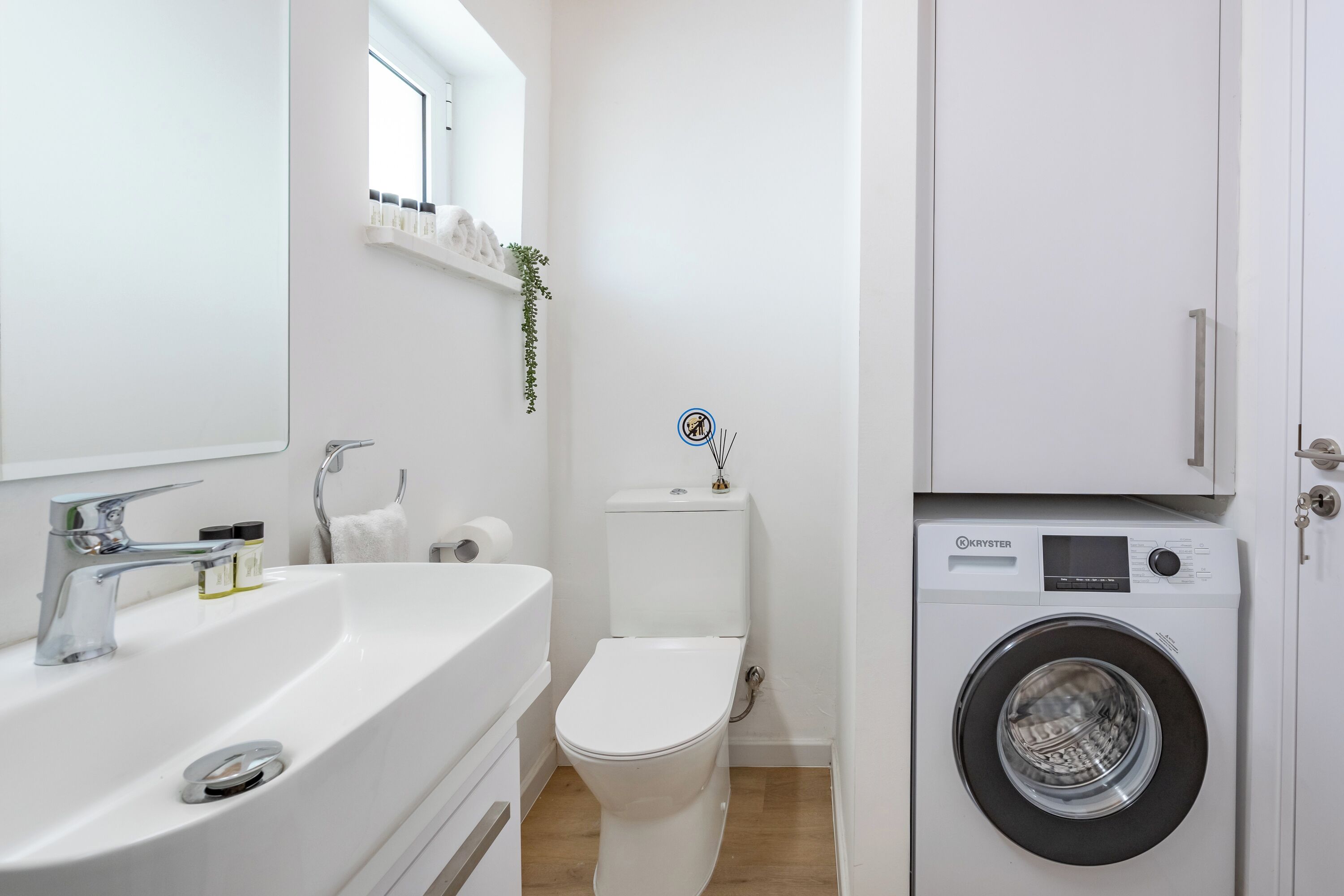 Un baño pequeño con lavabo blanco, inodoro y lavadora de carga frontal.