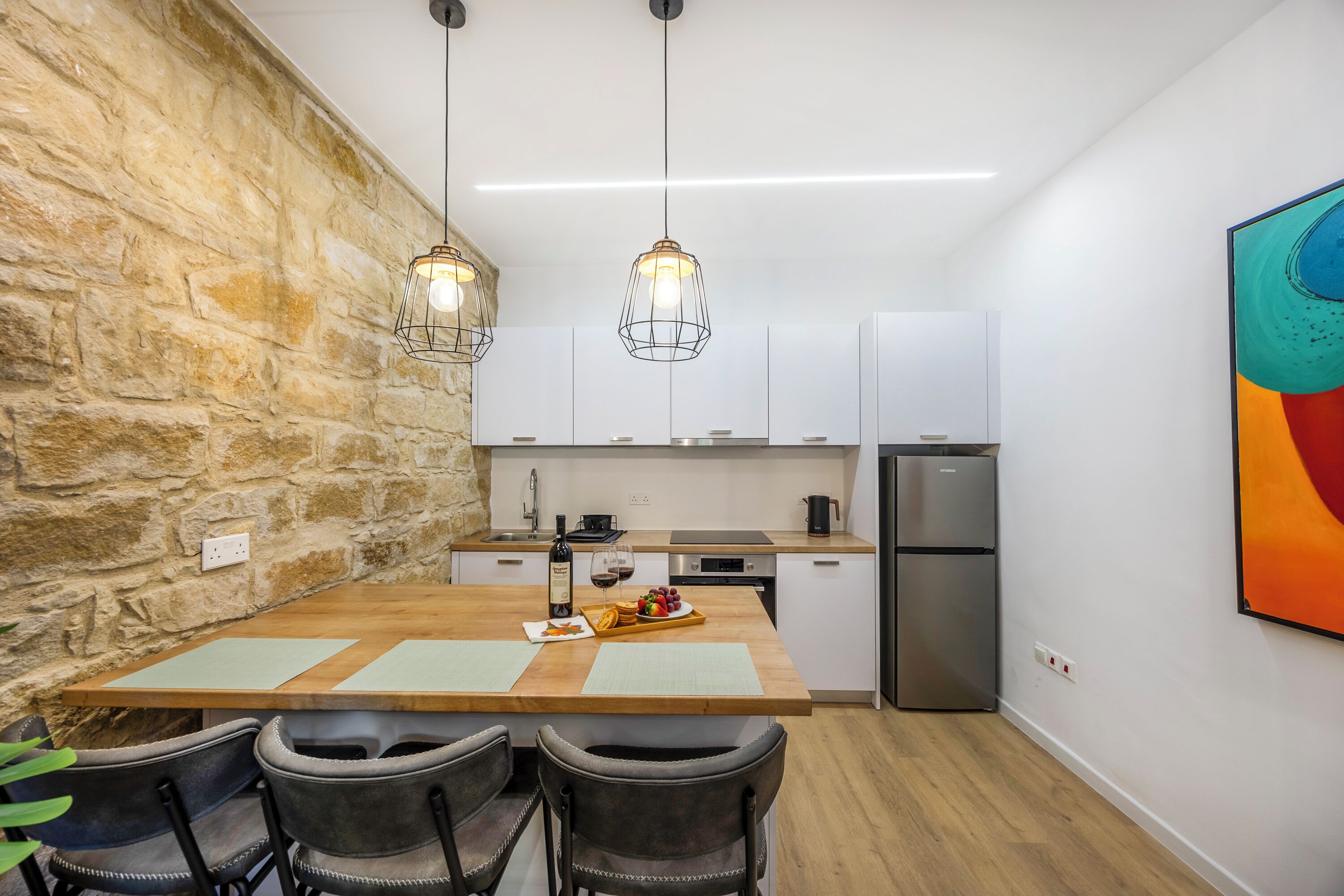 A modern kitchen with a wooden table, chairs, and pendant lights.