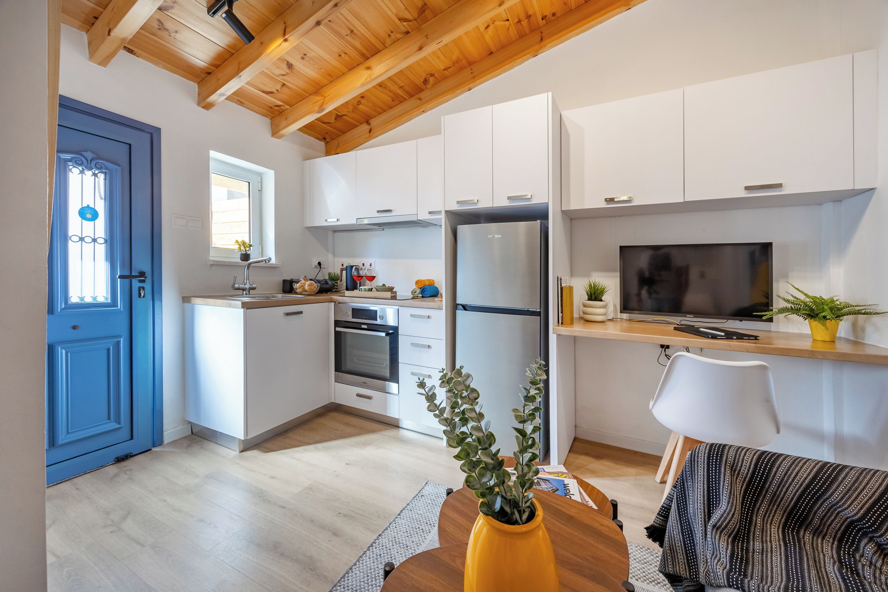 Una cocina moderna con armarios blancos, un refrigerador de acero inoxidable y techo de madera.