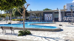 Una piscina pubblica con bordo in pietra, una panchina e un'area relax coperta.