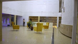Een ruime lobby met een hoge plafond, gele stoelen, een potplant en een receptiebalie.