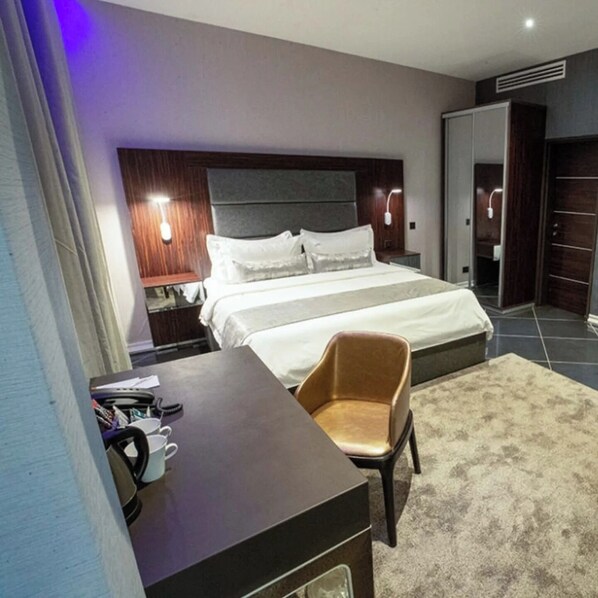 A hotel room with a bed, bedside tables, a desk, a chair, and a wardrobe.