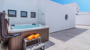 Una terraza en la azotea con un jacuzzi, cubierta de madera y un cielo azul despejado.