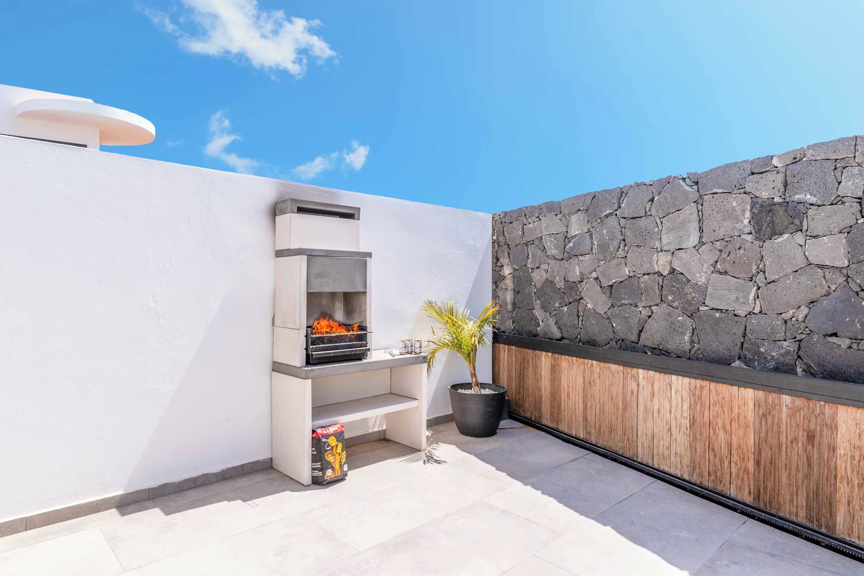 A rooftop patio with a stone wall, a grill, and a potted plant.
