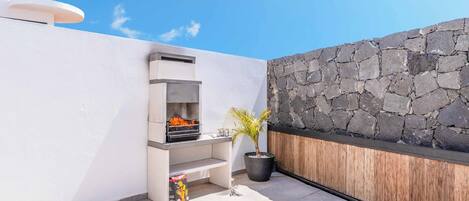 A rooftop patio with a stone wall, a grill, and a potted plant.