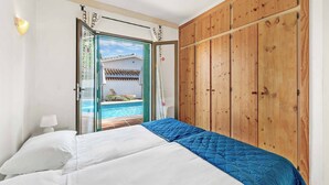 A bedroom with a bed, wooden wardrobe, and a view of a swimming pool. - Villa Bart - Four Bedroom Villa, Sleeps 8 (Bel-Air)