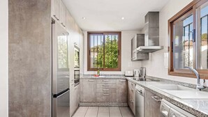 A modern kitchen with a built-in washing machine, stainless steel appliances, and a window with a view of greenery. - Villa Bart - Four Bedroom Villa, Sleeps 8 (Bel-Air)