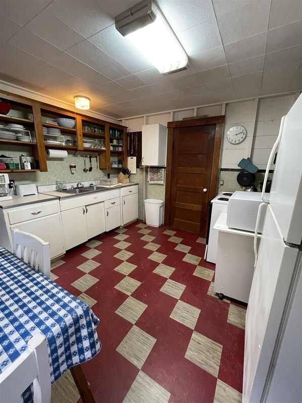 Una cocina pequeña con armarios blancos, piso a cuadros rojo y beige, y una puerta de madera.