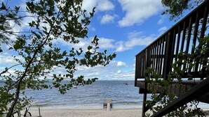 Eine Betonstaircase führt zu einer Holzterrasse mit Blick auf einen Strand, auf der sich eine Bank und ein Kajak befinden.