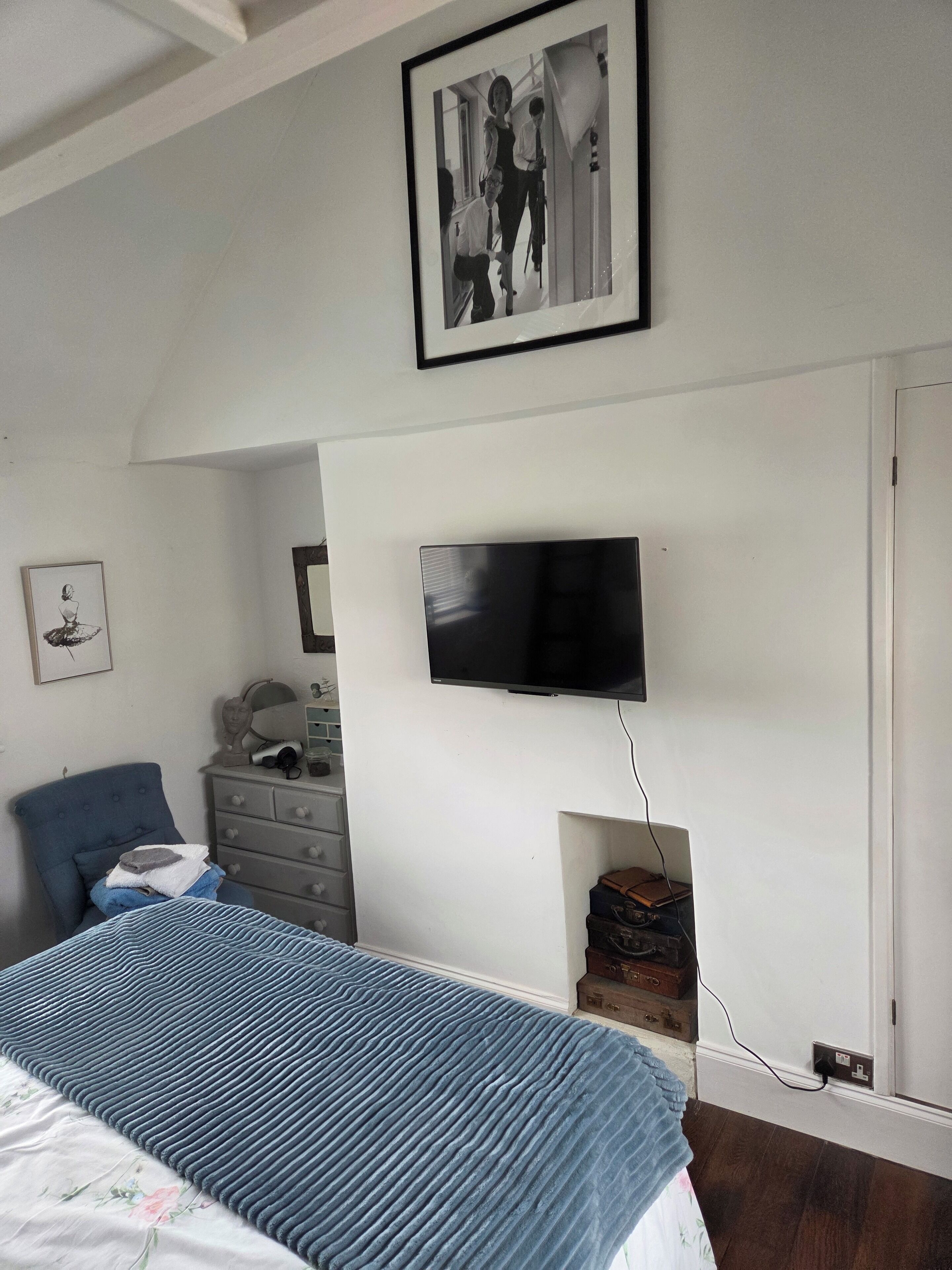 A bedroom with a bed, a dresser, a television mounted on the wall, and a framed picture above the bed.