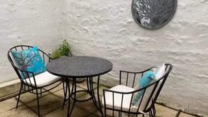 A patio with a round table and two chairs, a wall-mounted tree decoration, and a potted plant. - Beautiful Townhouse in Brighton's Regency Conservation Area (Brighton and Hove)