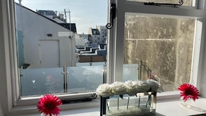 A window with a view of buildings, a clear sky, and a flower arrangement on the windowsill. - Beautiful Townhouse in Brighton's Regency Conservation Area (Brighton and Hove)
