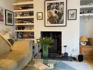 Una sala de estar con sofá, una mesa de centro con un libro, chimenea, estantería y cuadros en la pared.