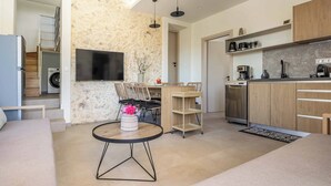 Ein modernes Wohnzimmer mit Sofa, Couchtisch, Fernseher und Küchenzeile mit Schränken und Geräten.