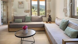 Ein modernes Wohnzimmer mit einer Couch, einem runden Tisch mit Blumenvase und Blick auf die Landschaft durch ein großes Fenster.