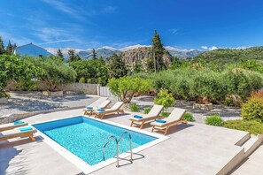 Une piscine rectangulaire avec un escalier en métal, entourée de chaises longues dotées de coussins bleus.