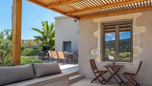 Eine überdachte Terrasse mit einer Holz-Pergola, einer Sitzecke mit gepolstertem Sitz und einem Tisch mit zwei Holzstühlen.
