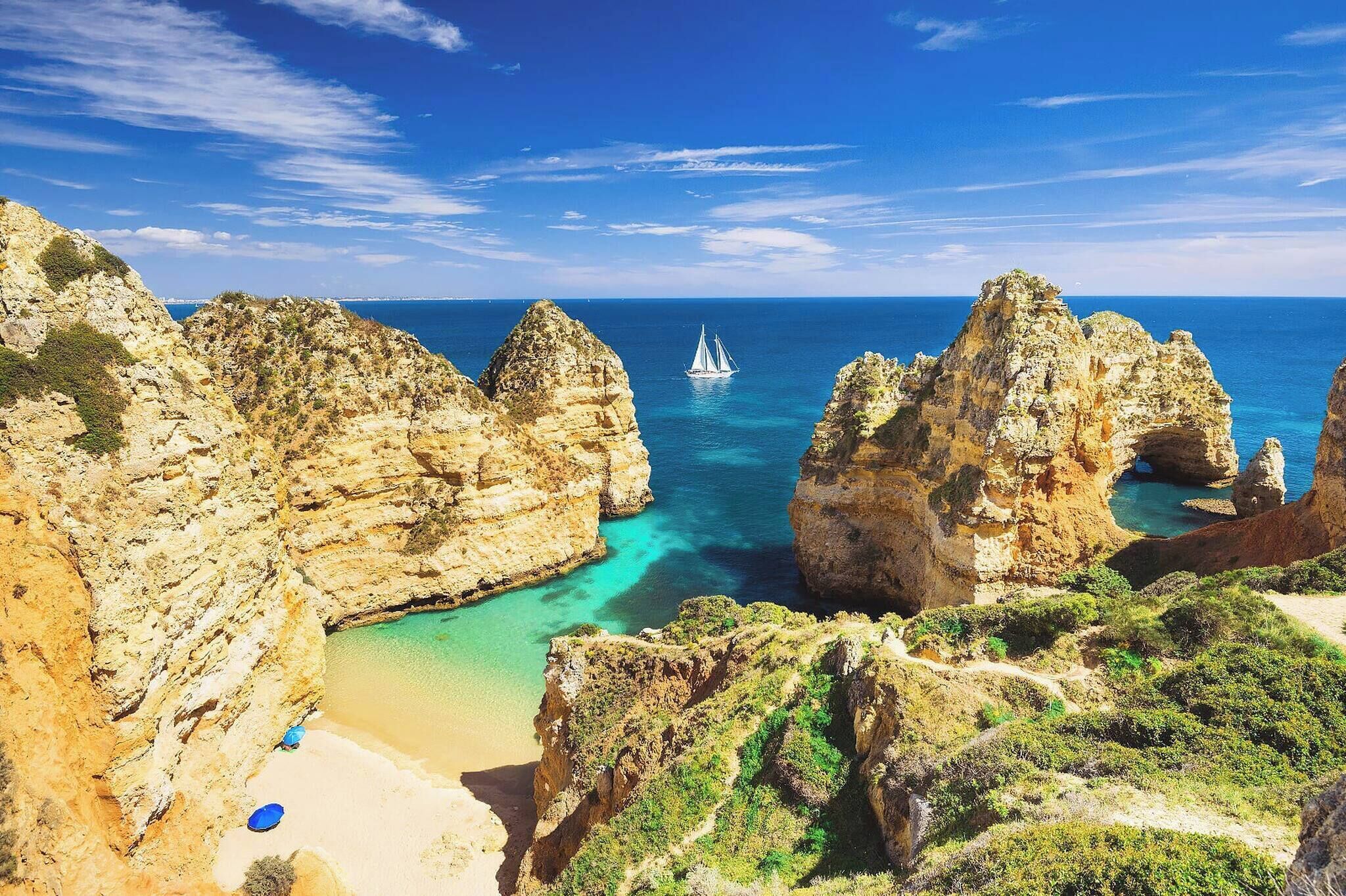 A coastal landscape with rocky cliffs, a beach, and a sailboat in the distance.
