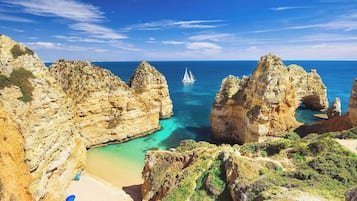 A coastal landscape with rocky cliffs, a beach, and a sailboat in the distance.