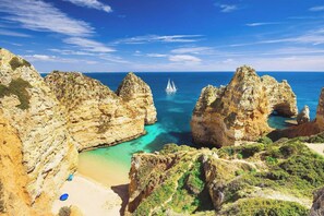A coastal landscape with rocky cliffs, a beach, and a sailboat in the distance. - New, Nature View - Albufeira, Private Pool (Albufeira)