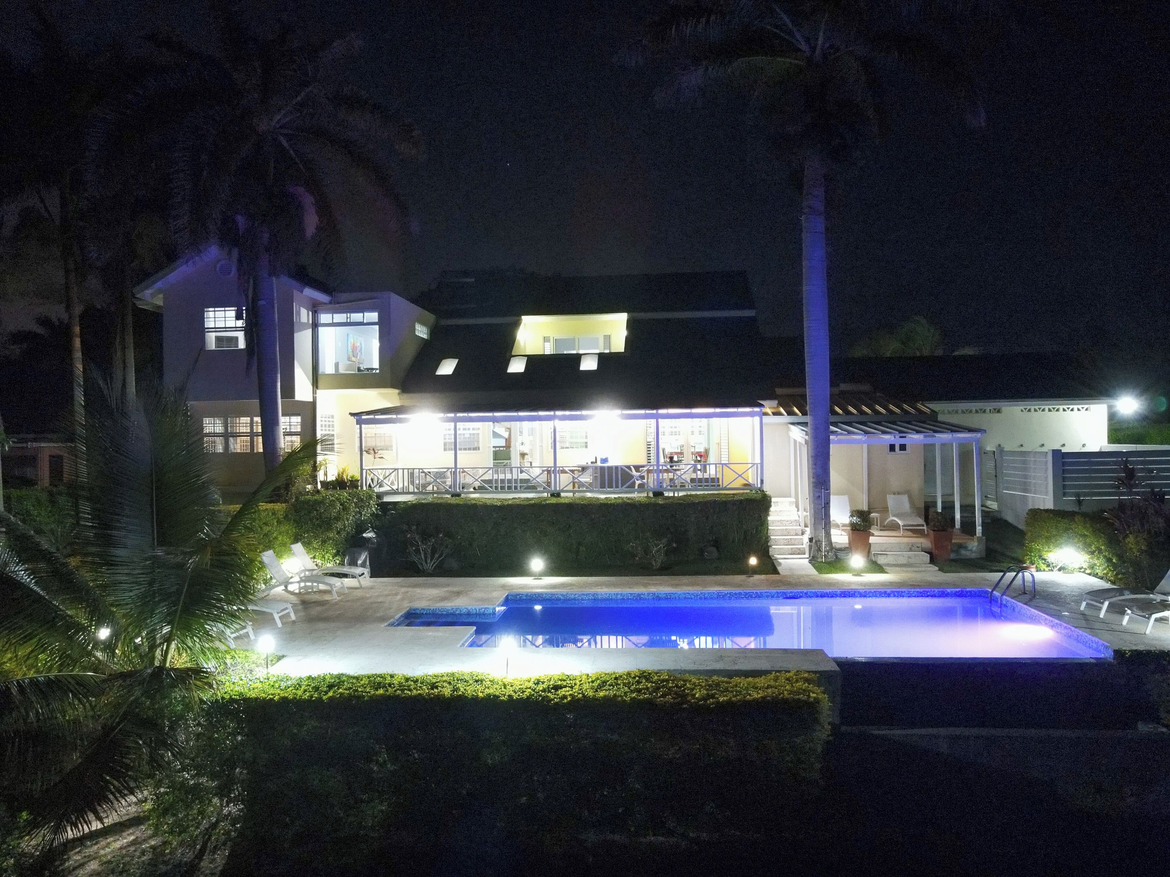 Een modern huis met een zwembad, een overdekt terras en een goed verlichte gevel 's nachts.