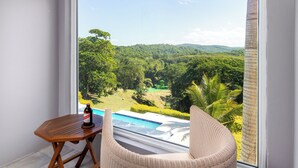 Un balcon donnant sur un paysage verdoyant, une table en bois avec une bouteille et une chaise en osier.