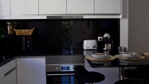 A modern kitchen with white cabinets, a black countertop, a toaster, a kettle, and a dining area with a table set for two. - Golden Moon, Ponta do Sol - Canhas (Funchal)