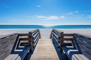 A wooden boardwalk leading to a beach with a clear blue sky.