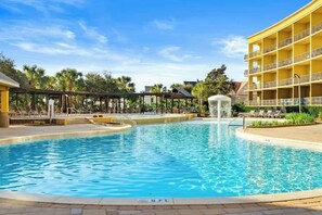 A swimming pool with a water fountain, lounge chairs, and a multi-story building in the background.