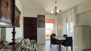 A dining area with a table and chairs, a chandelier, and a view of the outdoors through a door. - Delux-The Terrace Over The Marine Park (Quartu Sant'Elena)