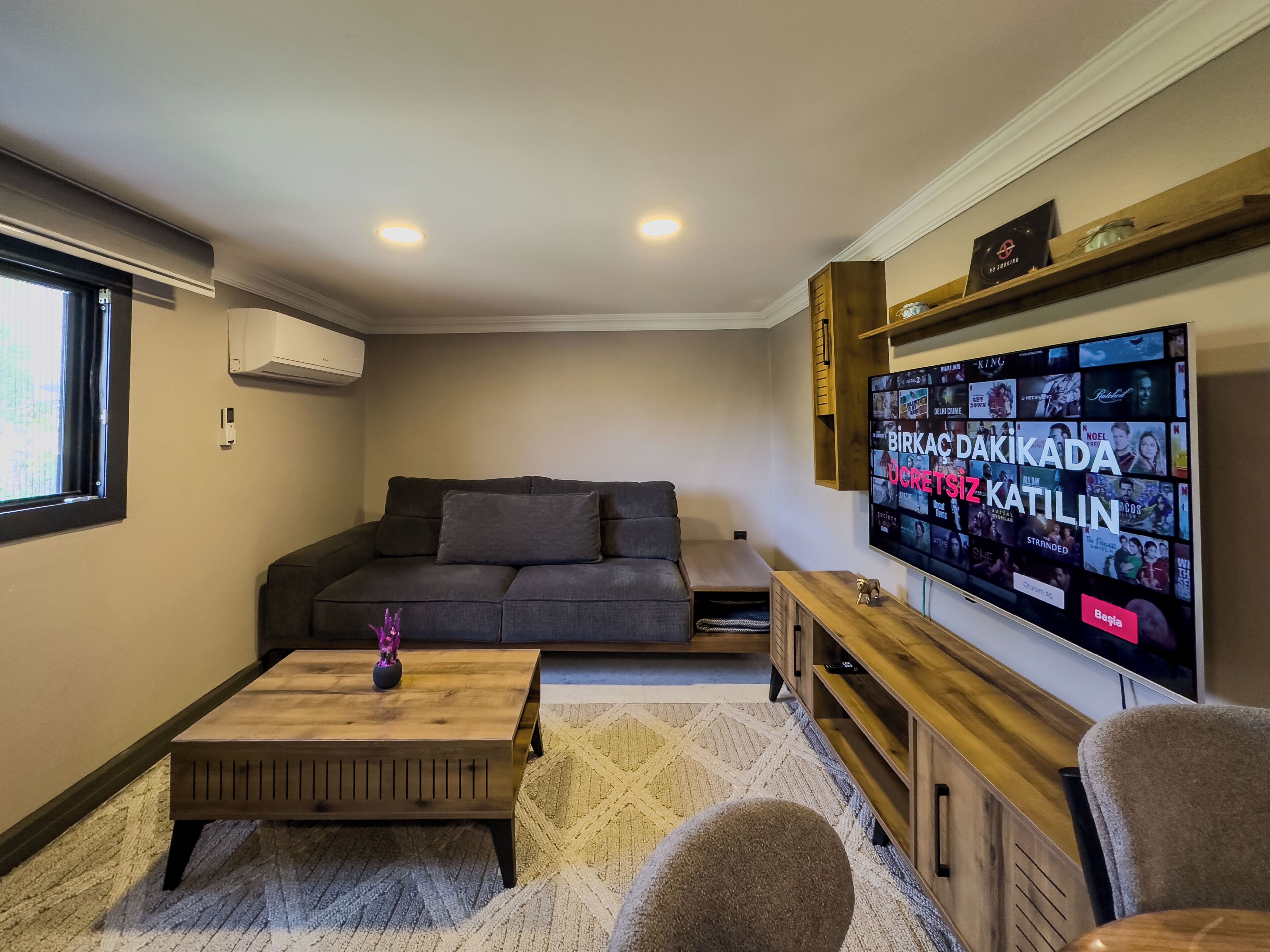 A living room with a grey sofa, a wooden coffee table, and a TV mounted on the wall displaying various streaming services.