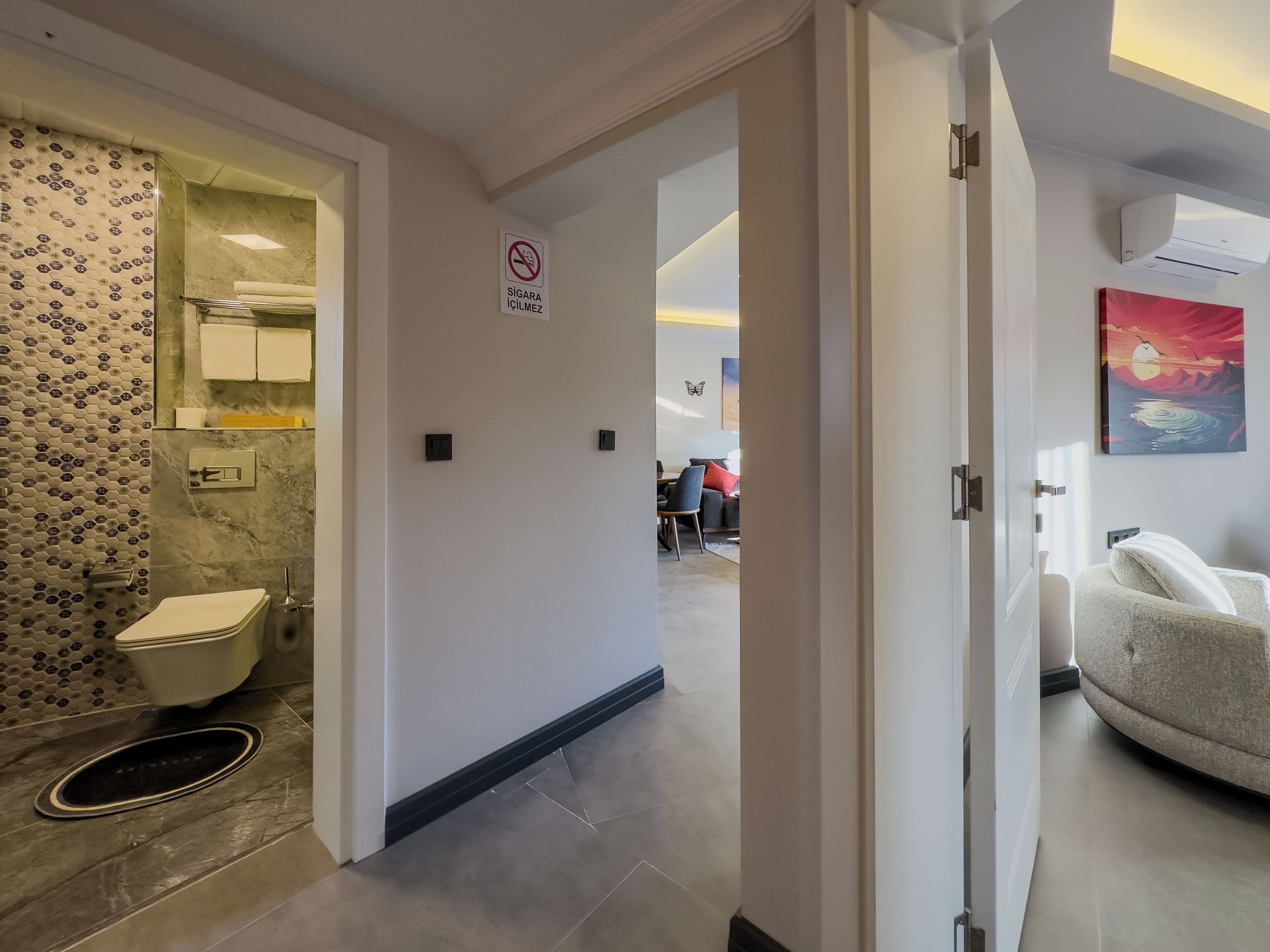 Ett hotellbadrum med toalett, handfat och dusch. Det finns en skylt som visar att rökning inte är tillåtet. Badrummet har mönstrade kakelplattor och en modern design.