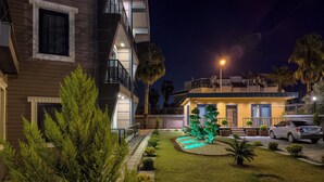 A modern multi-story building with a well-maintained garden and a car parked in front. - Belek 07 Luxury Suites Only For Family (Serik)
