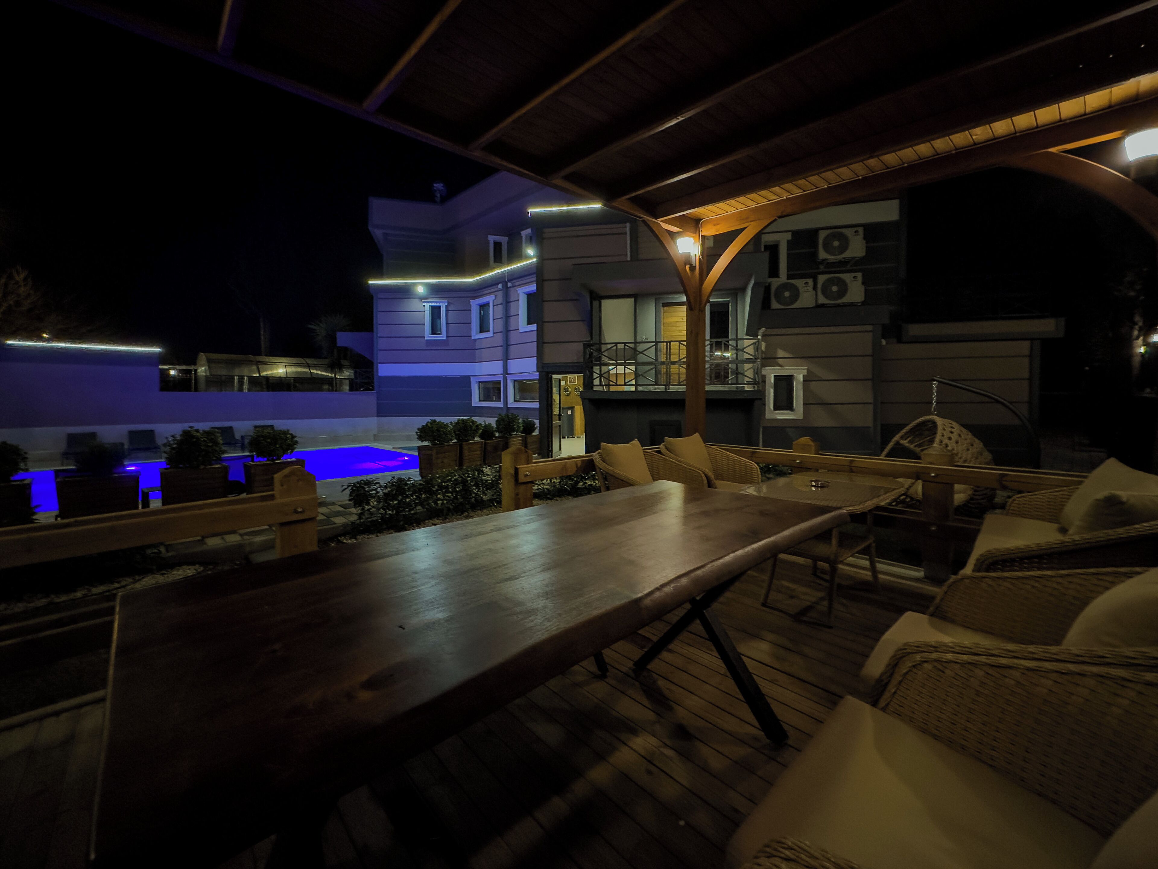 Un patio al aire libre con piscina, mobiliario de madera y un edificio moderno al fondo.