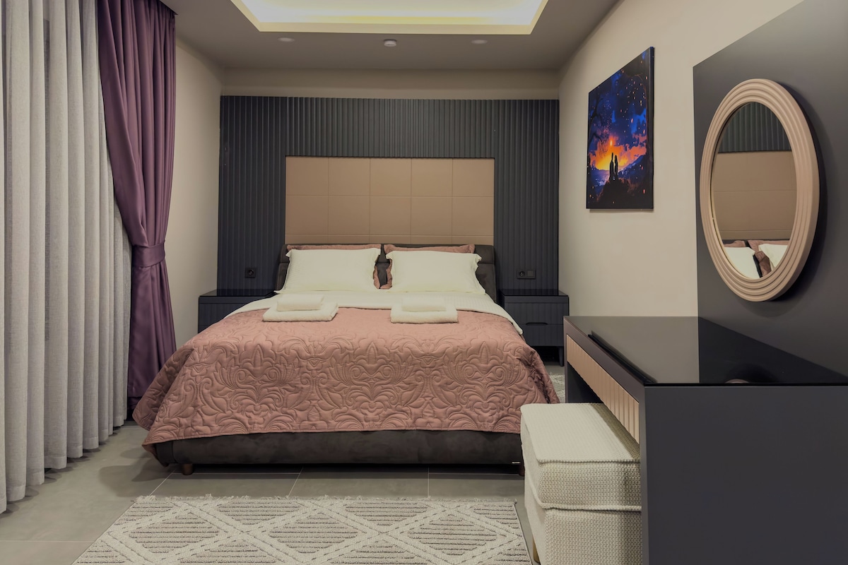 A modern bedroom with a large bed, bedside tables, a nightstand, a mirror, and a painting on the wall.