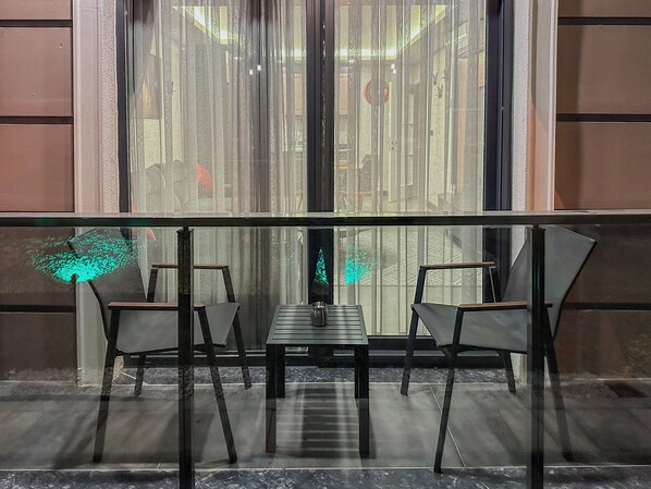 A modern interior with a glass railing, two chairs, a table, and a view through a large window with sheer curtains. - Belek 07 Luxury Suites Only For Family (Serik)