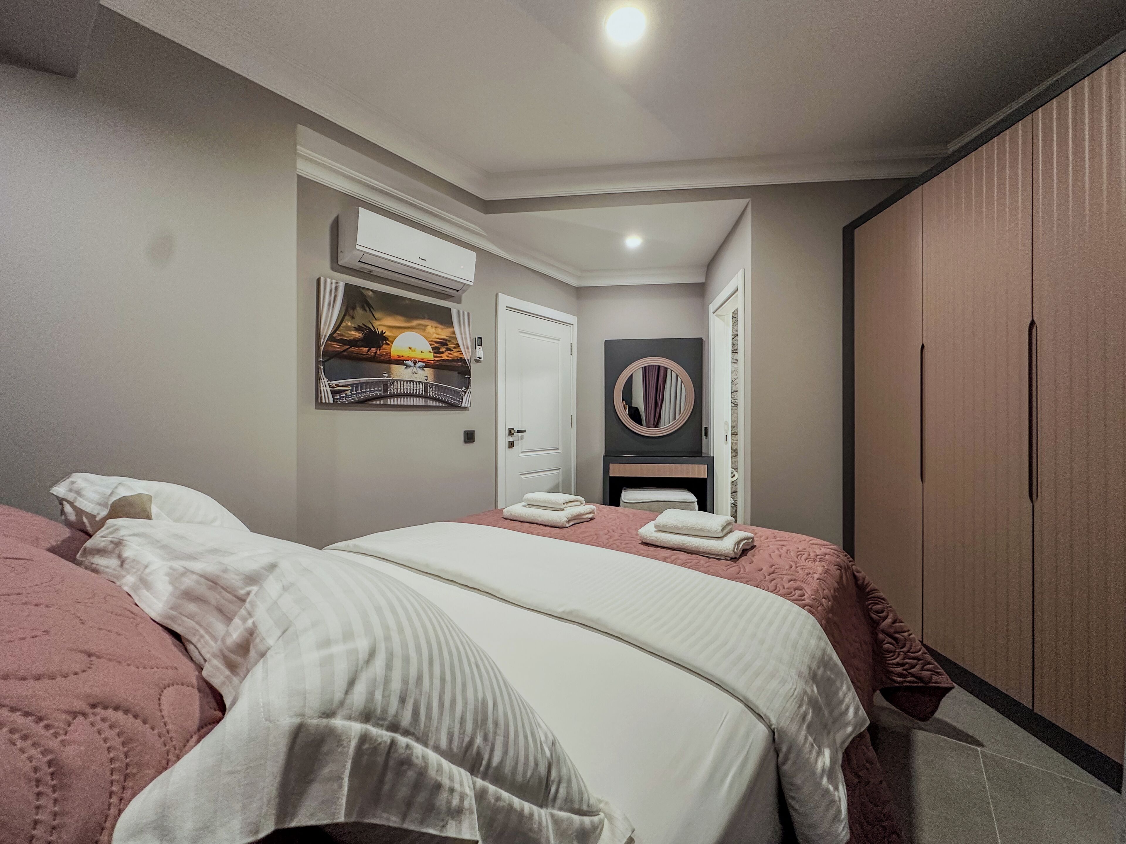 A hotel room with a bed, a wardrobe, a mirror, and a painting on the wall.