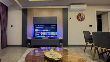 Ein modernes Wohnzimmer mit einem an der Wand befestigten Flachbildfernseher, einem runden Couchtisch mit dekorativer Schale und zwei Sessel.