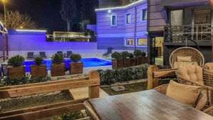 A modern outdoor pool area with wooden deck seating and planters, surrounded by a well-lit building with a balcony. - Belek 07 Luxury Suites Only For Family (Serik)