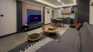 A modern living room with a flat-screen TV, a sofa, a coffee table, and a dining area with chairs. - Belek 07 Luxury Suites Only For Family (Serik)