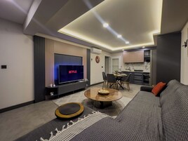 Una sala moderna con un televisor de pantalla plana, un sofá, una mesa de centro y un comedor con sillas.