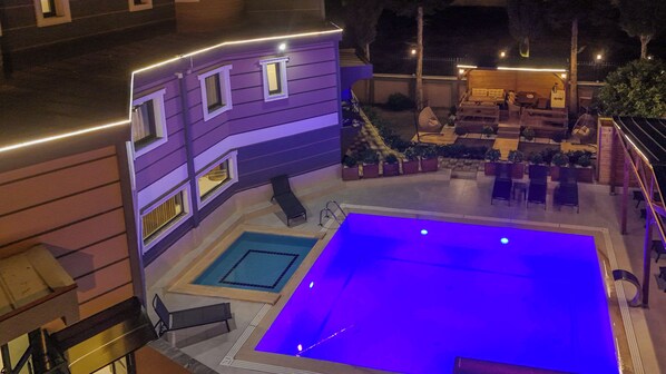 A rooftop pool area with a small pool and a larger pool, surrounded by lounge chairs and a wooden deck.