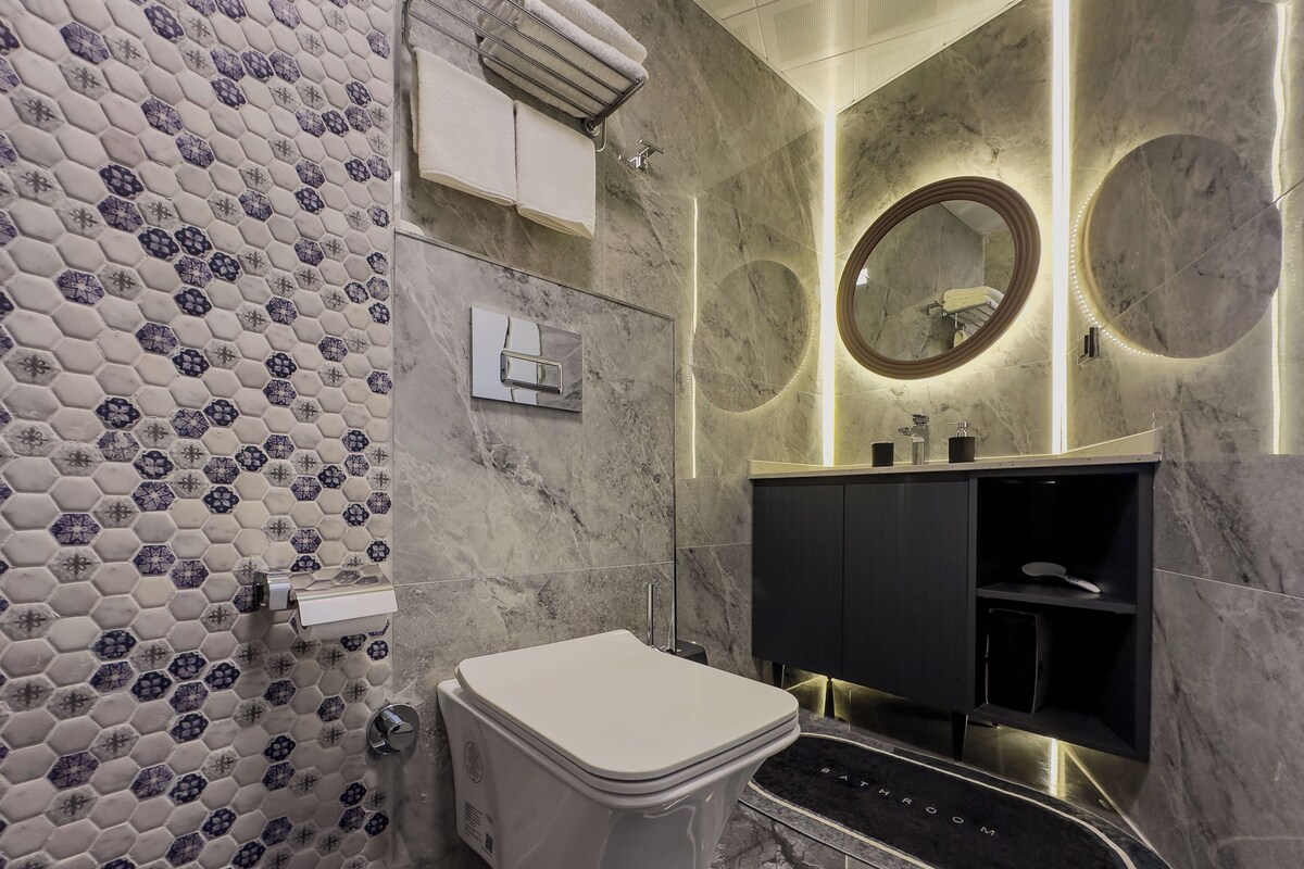 A modern bathroom with a hexagonal tile backsplash, a white toilet, a black vanity with a mirror, and a heated floor mat labeled "BATHROOM".
