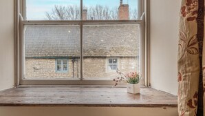 A window with a view of a brick building, a small potted plant on the windowsill, and a curtain partially visible on the right. - Eilmers Cottage - Beautiful 4BD in Malmesbury (Malmesbury)