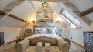 A bedroom with a large bed, a decorative mirror, two bedside tables, a dresser, and a sloped ceiling with exposed beams. - Eilmers Cottage - Beautiful 4BD in Malmesbury (Malmesbury)